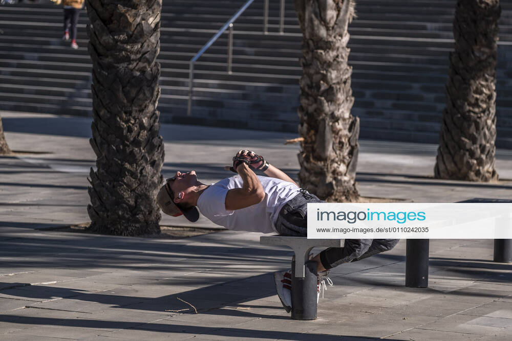 A man wearing sportswear is seen doing sit-ups using street furniture in the Plaza de la Rosa de los Vientos..With public sports centers and gyms closed due to the increase in Covid-19 infections, many individual and social sports activity is taking place in public space such as open areas near the beaches. Barcelona Spain - ZUMAs197 20210117_zaa_s197_065