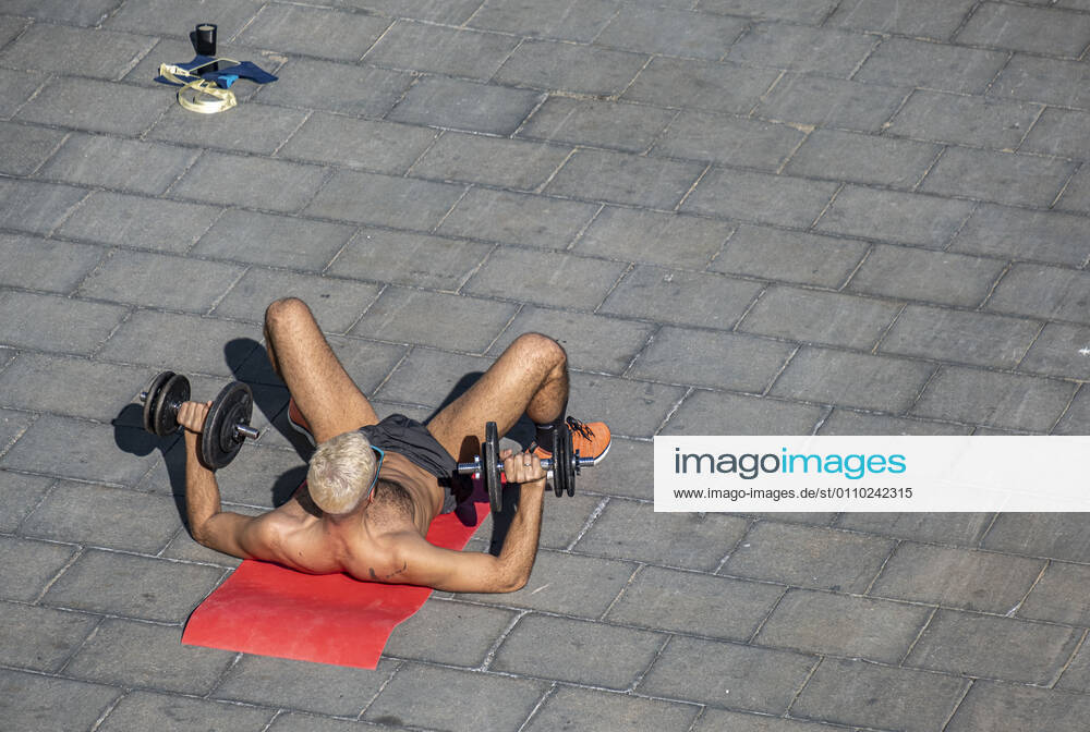 A man wearing shorts and with a bare torso is seen on the ground practicing bodybuilding on Passeig del Mare Nostrum..With public sports centers and gyms closed due to the increase in Covid-19 infections, many individual and social sports activity is taking place in public space such as open areas near the beaches. Barcelona Spain - ZUMAs197 20210117_zaa_s197_069