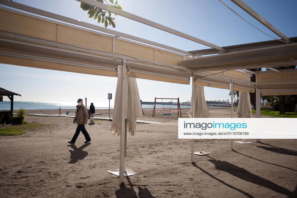 A man wearing a face mask as a precaution against the spread of covid-19 walks past a closed beach bar at La Malagueta beach amid coronavirus pandemic..The region of Andausia suffers an uncontrolled daily rise of coronavirus cases, despite of hard restrictions imposed in the daily life. During the last weeks, Andalusia has reported thousands of infections everyday in the region while the hospital pressure continue rising. Malaga Spain - ZUMAs197 20210122_zaa_s197_040