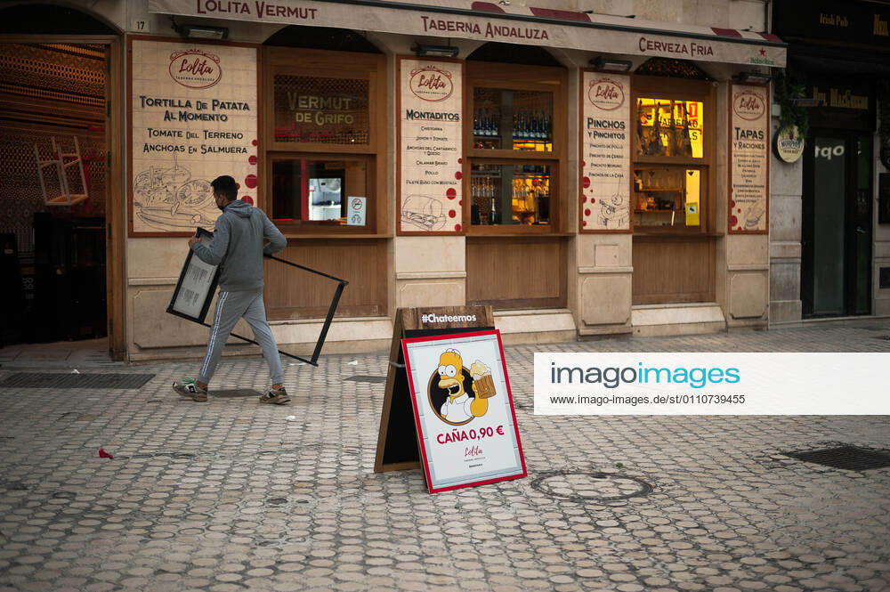 A poster with the image of character Homer Simpson offering beers seen outside Lolita Vermut bar as an employee carries a board during the mandatory closure..The third wave of coronavirus disease has impacted most daily income in the Andalusia region after the Christmas holidays. Following the increase of infections, several regional governments decided to take new measures such as limiting mobility perimeters between cities and towns and closing hospitality and commercial sectors in the afternoon. Malaga Spain - ZUMAs197 20210122_zaa_s197_081