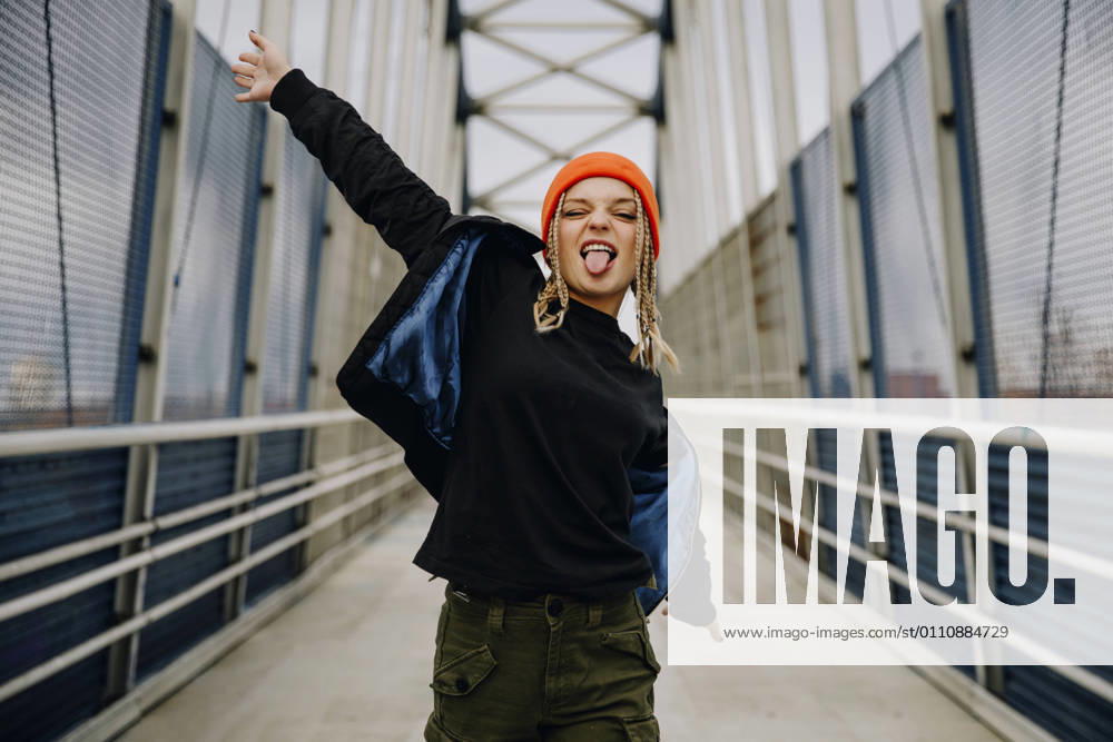 Happy young woman with eyes closed sticking out tongue while dancing on footbridge model released Symbolfoto ACPF00989
