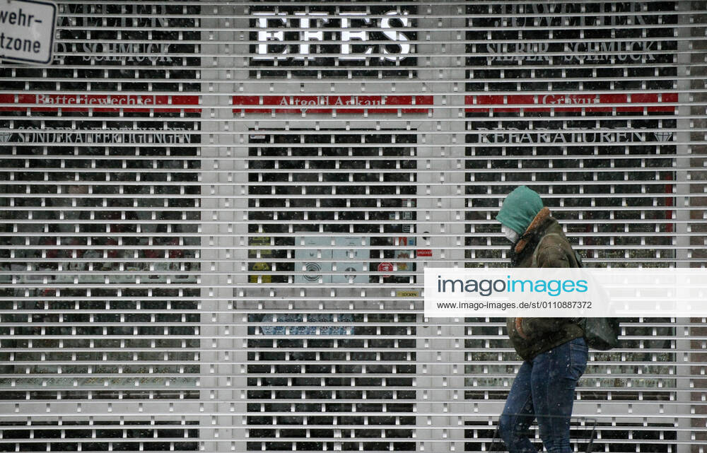 Winter wetter mit Schnee , a women with Safety mask FFP2 is seen under the snow as she walks beside a closed shop during the Hard Lockdown of the Covid 19 Coronavirus Pandemie in Nuremberg Nurnberg , Bayern , Deutschland . January 24 , 2021.