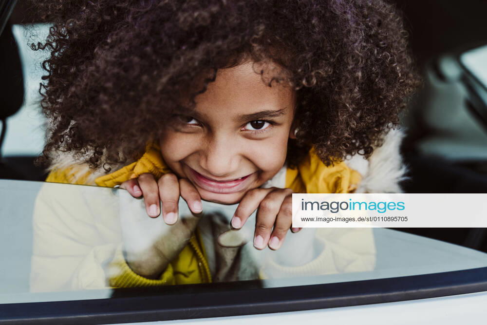 Close-up of smiling girl with curly hair peeking through car window model released Symbolfoto EBBF01987