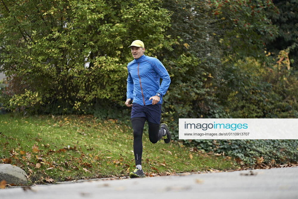 Mature man in sports clothing running on footpath by grass model released Symbolfoto JAHF00073
