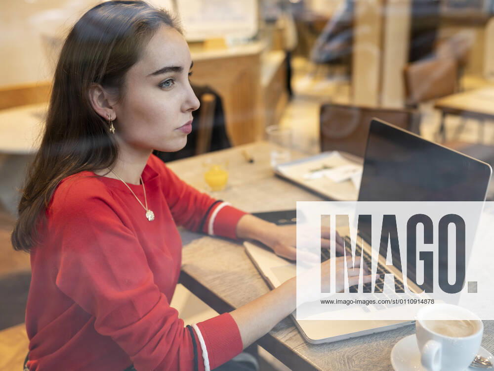 Thoughtful woman with laptop seen through glass of cafe model released Symbolfoto JCCMF00247