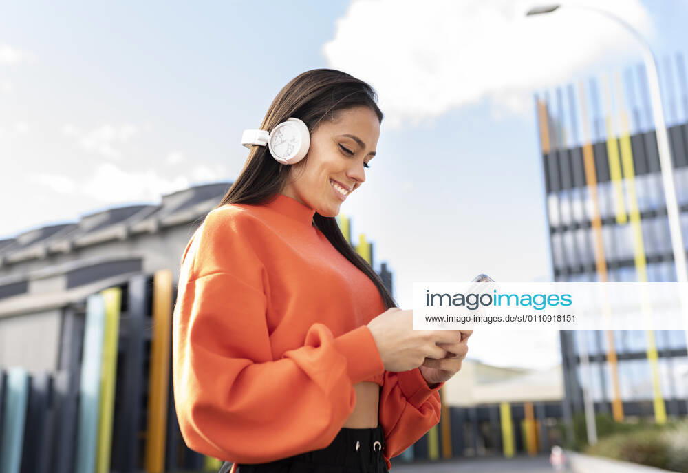 Portrait of beautiful brunette standing outdoors and smiling while listening to music on headphones model released Symbolfoto JCCMF00754