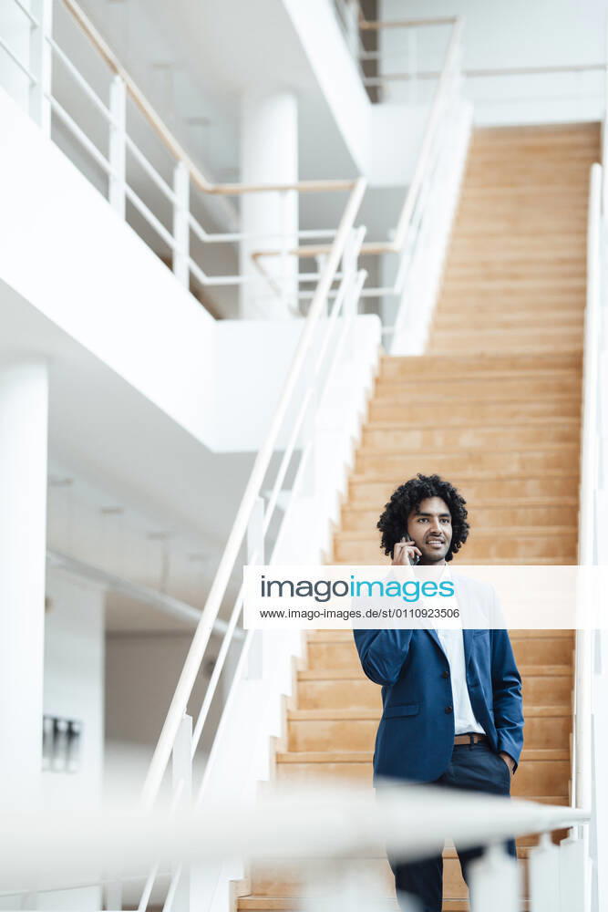 Young male professional talking on mobile phone while looking away against staircase in office model released Symbolfoto property released JOSEF02956