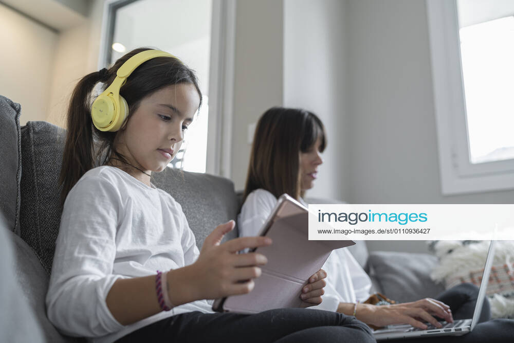 Daughter holding digital tablet while mother using laptop sitting by at home model released Symbolfoto property released SNF00913