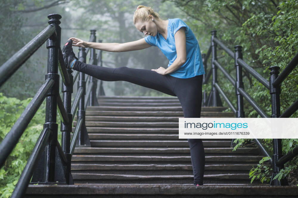 Female athlete stretching on stairs in public park on rainy mist Montreal, QC, Canada CR_CHPH210119B-613054-01 ,model released, Symbolfoto