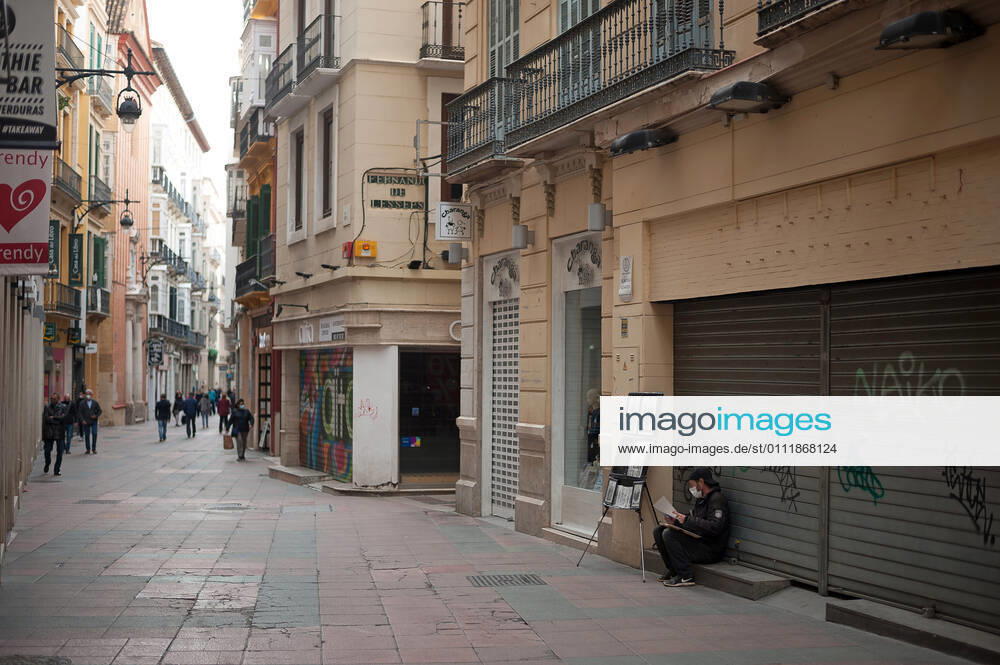 A street painter wearing a face mask as a precaution against the spread of covid-19 seen sitting in front of a closed store as people walk along an empty and deserted Nueva street amid the partial lockdown caused by coronavirus pandemic. Malaga Spain - ZUMAs197 20210203_zab_s197_007