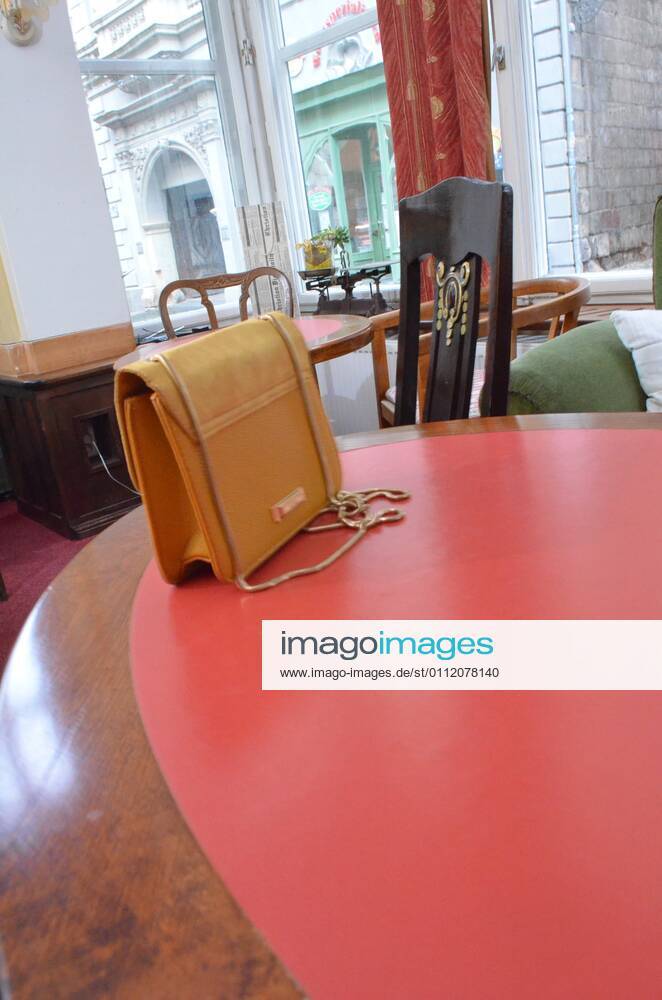 A young woman in a yellow jacketand a green dress sits with a yellow handbag in a cafe restaurant symbol photo