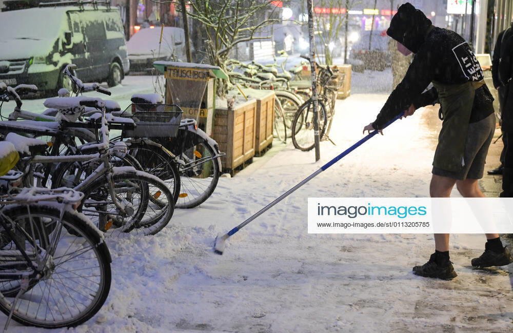 DEUTSCHLAND, Hamburg, Winter, Ladenangestellter in kurzer Hose befreit öffentliche Wege vom Schnee Hamburg Germany