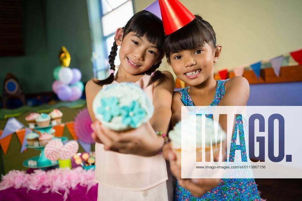 IMAGO Creative: Gesellschaft, Schule, Schulanfang Kids having cupcake during birthday party at home Portrait of kids having cupcake during birthday party at home, model released, , property released, Cape Town, South Africa, 2017-04-24T23:00:00.000Z, 1049243.jpg, home, house, household, homey, apartment, domicile, abode, living room, birthday, birthday party, party, anniversary, event, casual clothing, party hat, standing, smiling, happy, cheerful, holding, cupcake, sweet food, dessert, tasty, delicious, adorable, cute, childhood, innocence, friend, friendship, together, bonding, celebration, leisure, lifestyle Child, Girl, Female, Chinese, Mixed-Race, 8-9 Years, Girls, Chinese Ethnicity, Mixed-Race Person Indoors,Portrait,Looking at camera,Half length