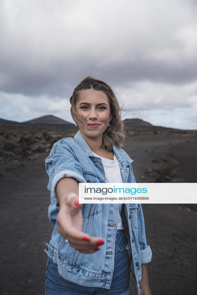 Smiling woman stretching hand while standing on footpath at Volcano El Cuervo, Lanzarote, Spain model released Symbolfoto SNF00999