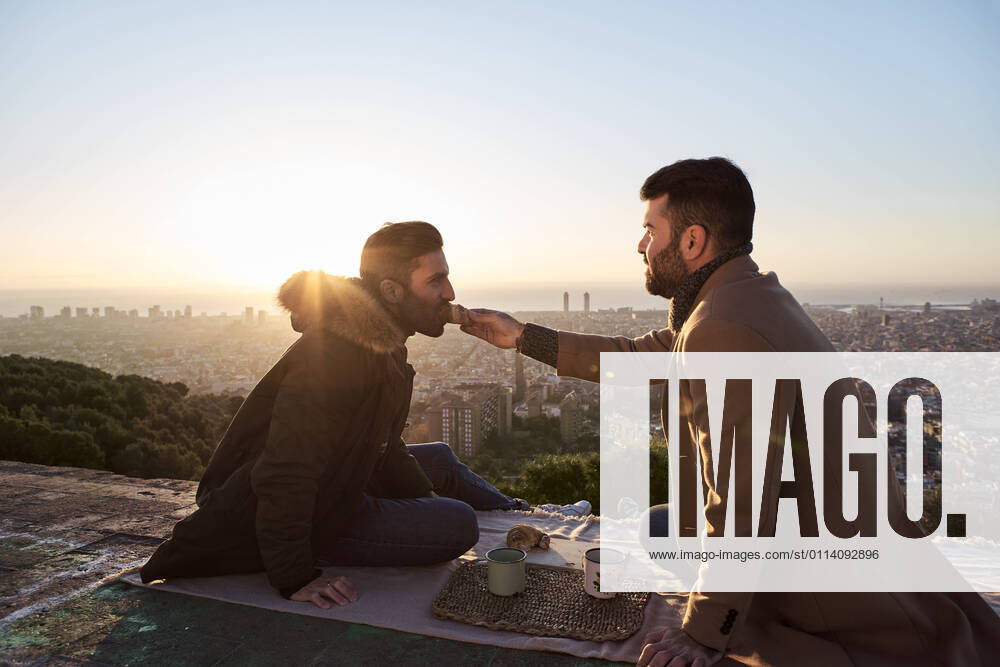Man feeding croissant to boyfriend while sitting on observation point against city, Bunkers del Carmel, Barcelona, Spain model released Symbolfoto VEGF03670