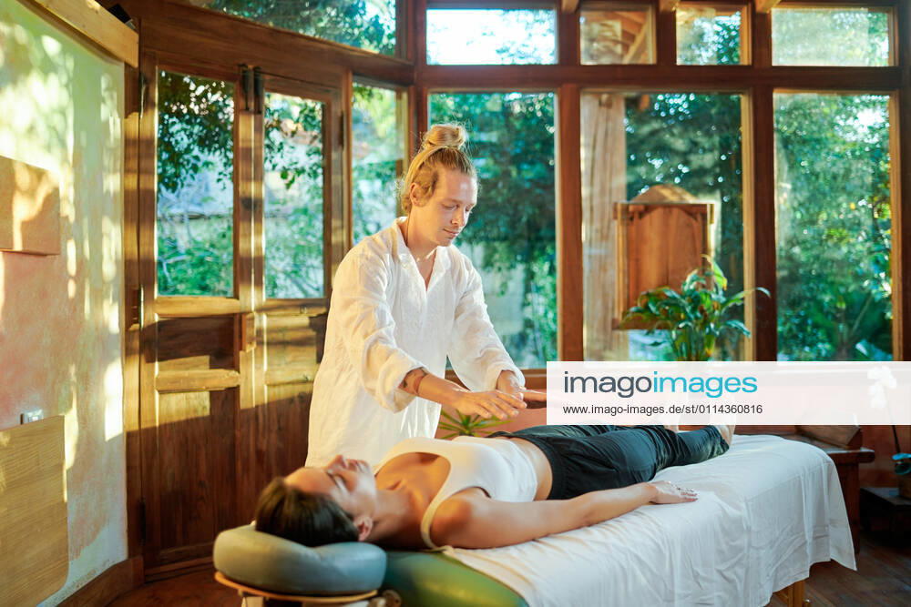 IMAGO Creative, Lifestyle, Esoterik gef?hrlicher Glaube Healer practicing palm healing technique for female client lying on couch during spiritual practice for filling with harmony and energy, Model released, Property released