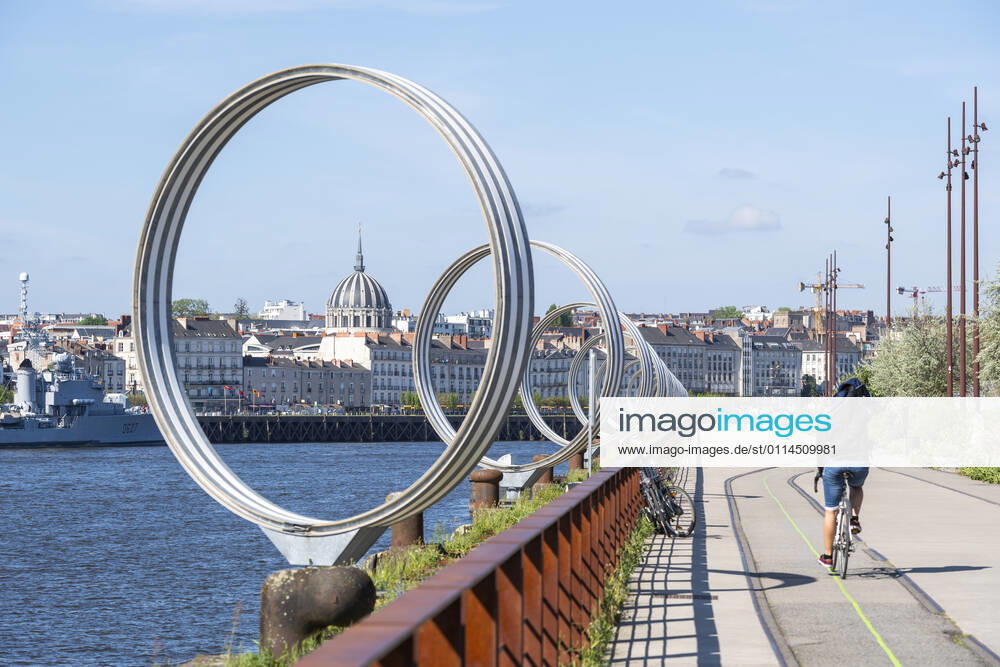Nantes (north-western France): the Rings by Daniel Buren on the quai des Antilles (West Indies quay) Nantes (north-western France): The Rings by Daniel Buren on the quai des Antilles (West Indies quay), along the Loire river on the ile de Nantes (Isle of Nantes). Cyclist on a cycle lane and overview of the city with the Church of Notre-Dame de Bon-Port (the artist s name must be mentioned, for press and edition use only) Pays de Loire; Atlantic Loire region; Nantes Europe; Western Europe; France