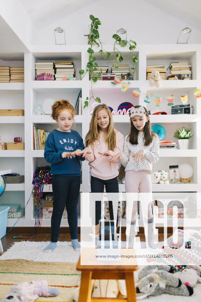 IMAGO Creative: Jahreszeit Winter, Fantasievoll drinnen spielen Full length of happy little girls in casual clothes standing in playroom against mobile phone while filming video of dance
