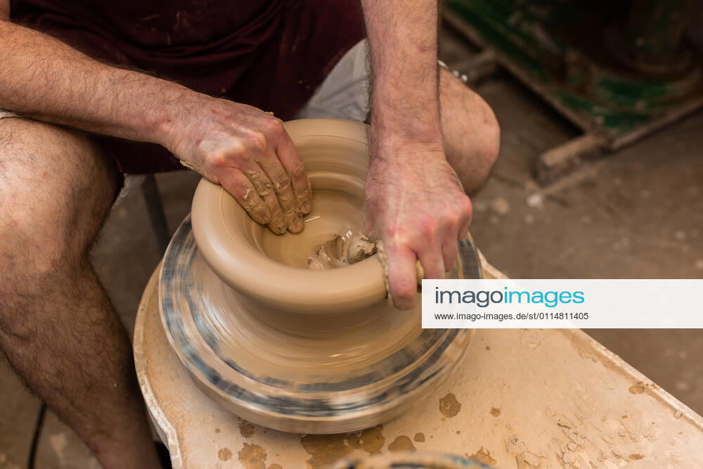 Crop unrecognizable sculptor with equipment giving shape while sculpting with brown clay on throwing wheel, Model released