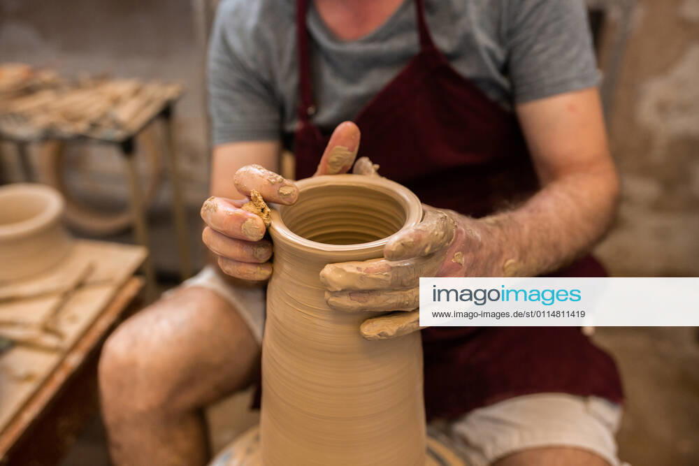 Crop unrecognizable sculptor with equipment giving shape while sculpting with brown clay on throwing wheel, Model released