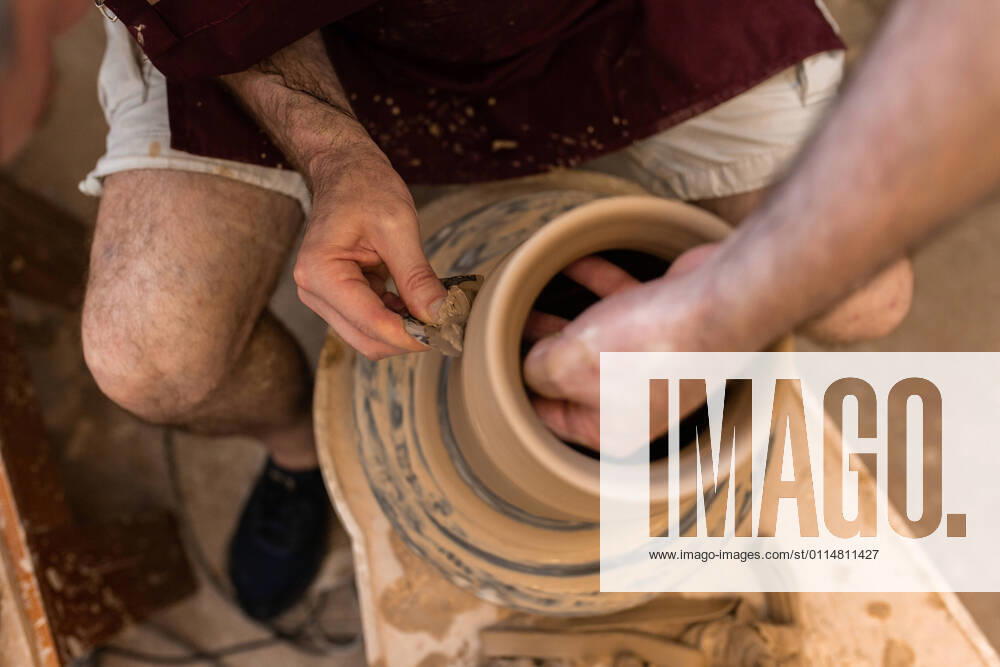 Crop unrecognizable sculptor with equipment giving shape while sculpting with brown clay on throwing wheel, Model released