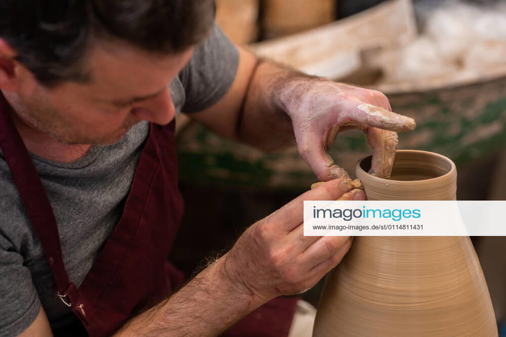 Crop unrecognizable sculptor with equipment giving shape while sculpting with brown clay on throwing wheel, Model released