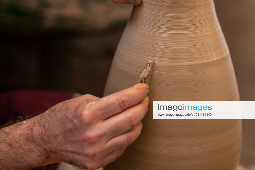 Crop unrecognizable sculptor with equipment giving shape while sculpting with brown clay on throwing wheel, Model released