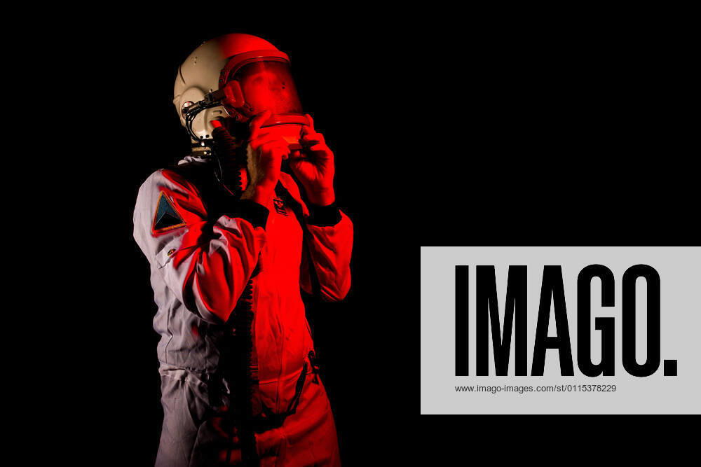 IMAGO Creative: 2022 Aussichten Male cosmonaut wearing white space suit and helmet while standing on black background in red neon light