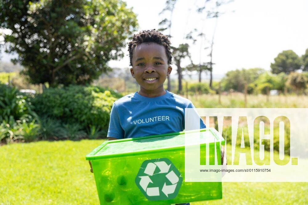 IMAGO Creative: Klimawandel - Umwelterziehung Volunteers collecting rubbish and recycling Front view of a smiling young African American boy standing in a field wearing a t shirt with volunteer written on it, holding a green plastic recycling crate and smiling to camera, model released, , property released, Cape Town, South Africa, 17.11.2019, 1297934.jpg, people,real people,home,domestic life,lifestyle,free time,leisure,relaxing,happy,enjoying,childhood,summer,nature,field,recycling,eco-friendly,green,volunteer,volunteering,environment,cleaning,awareness,education,learning,social responsibility,community,community spirit,helping,rubbish,collecting,trash,rural,countryside Child,Boy,Male,Black Outdoors,Front view,Close-up,Copy space,Looking at camera,Day,Half length