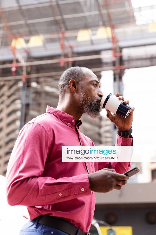 African American man using his phone and drinking takeaway coffee African American man out and about in the city streets during the day, wearing pink shirt and earphones, having a takeaway coffee and using a smartphone., model released, , property released, Cape Town, South Africa, 11.03.2020, 1334727.jpg, people,real people,commuting,commuter,travel,city,creative,individuality,lifestyle,street fashion,modern,on the go,digital nomad,independent,casual,street,coffee,to go,takeaway,cup,drinking,beverage,smartphone,mobile phone,technology,phone,holding,using,communication,connection,interacting Mature Adult,Man,Male,Black Outdoors,Side view,Day