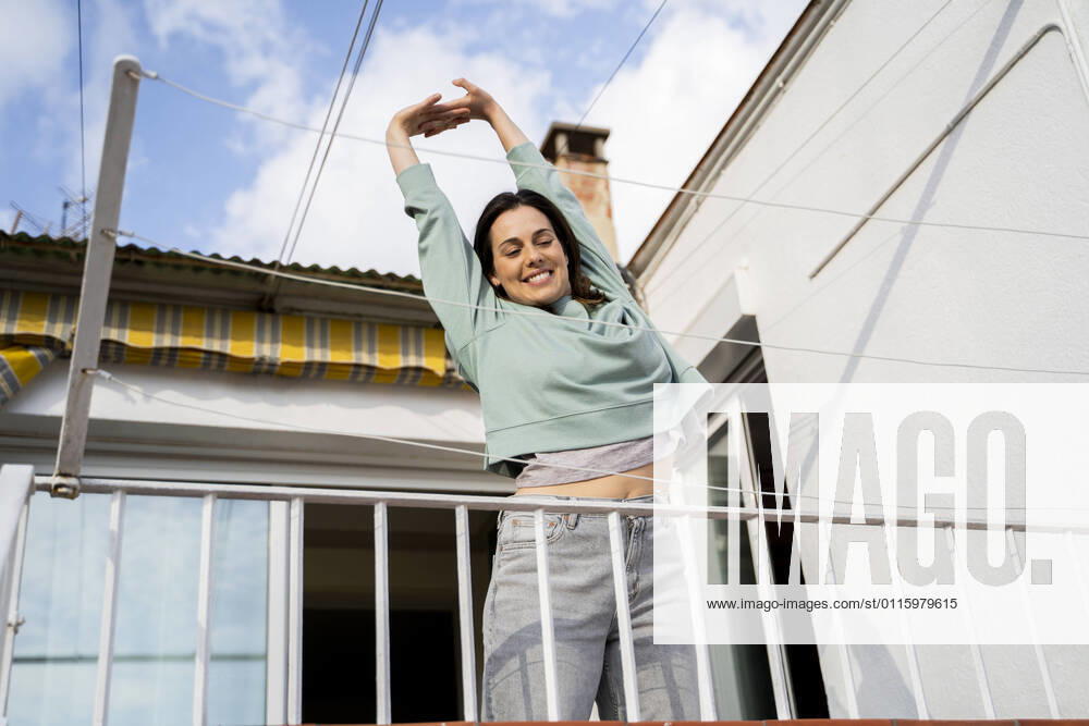 Smiling woman stretching hand while standing at balcony model released Symbolfoto property released AFVF08218