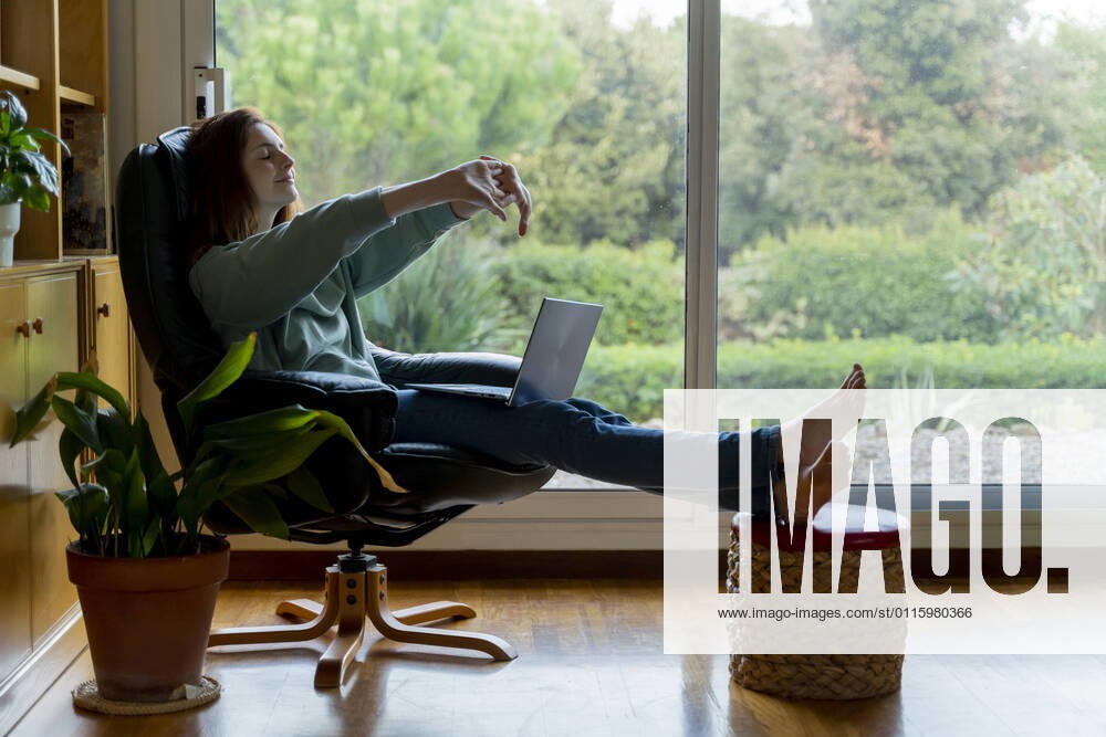 Mid adult woman stretching hand while sitting on chair at home model released Symbolfoto property released AFVF08326