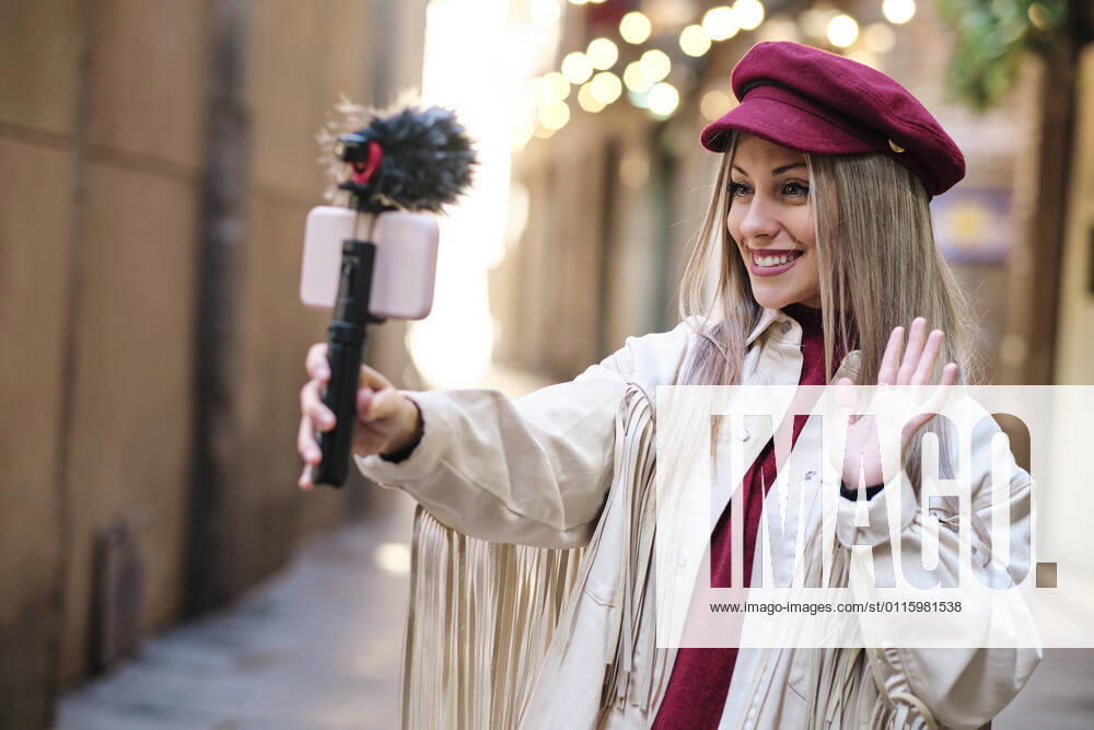 Smiling female vlogger waving hand while filming through mobile phone in city model released Symbolfoto AGOF00080