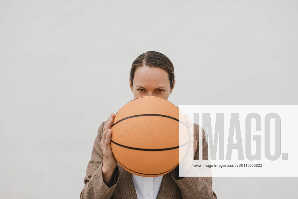 Businesswoman holding basketball in front of face against white wall during break model released Symbolfoto DMGF00515