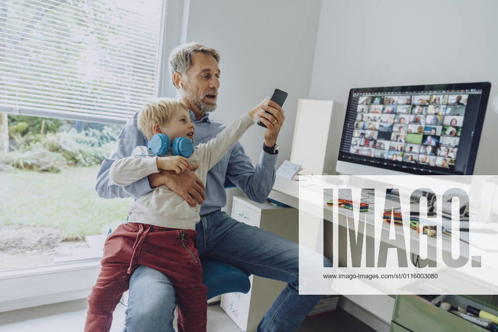 Son distracting father through smart phone while video conferencing at home office model released Symbolfoto property released MFF07200