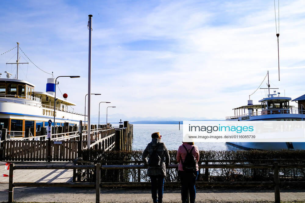 Spring weather at the Ammersee 25 03 2021 Excursionists in front of ships during spring weather in the harbour of Stegen Inning at the Ammersee Upper Bavaria with view towards the Alps Inning Bavaria Germany