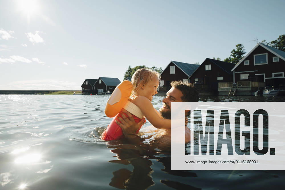 IMAGO Creative, Jahreszeit Sommer, Sommerferien IMAGO Creative: Vaterschaft IMAGO Creative: Dichotomien, Reflexionen Side view of cheerful daughter with father in lake during vacations Sweden, Tierp, model released
