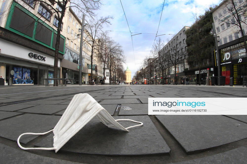 Worn mouth nose covering mask lies on the pavement of the deserted pedestrian zone and shopping street Planken in downtown Mannheim, Baden Württemberg, Germany