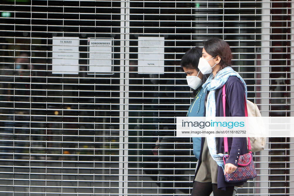Women wearing masks walk past a shop closed with a rolling gate during the lockdown in the shopping street pedestrian zone Planken in downtown Mannheim, Baden Württemberg, Germany