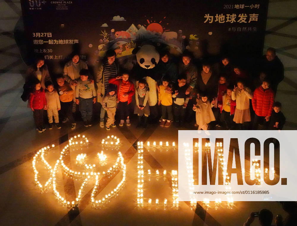 People pose with a giant panda and 60+ pattern formed by candles during Earth Hour 2021 on March 27, 2021 in Yantai, Shandong Province of China. Earth Hour 2021 is an environmental campaign organized by the World Wide Fund for Nature (WWF) to raise awareness of climate change by encouraging people to turn off lights for an hour.