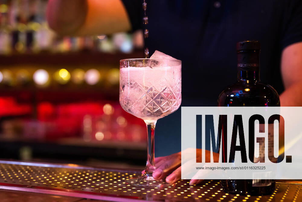 Young Asian bartender pouring tonic water to the glass for preparing a gin tonic cocktail in the bar