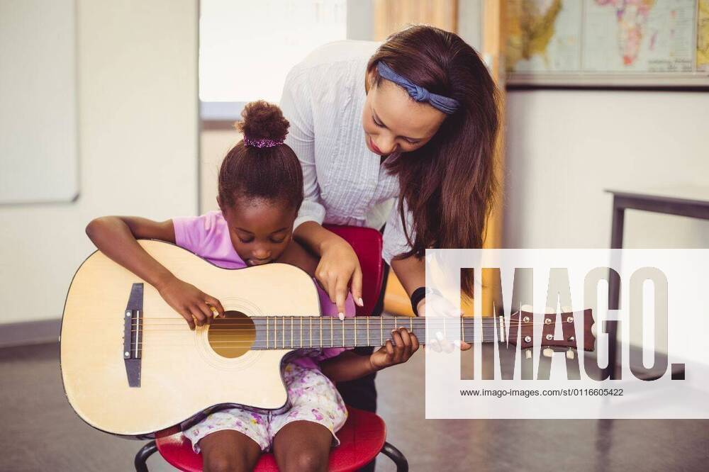 IMAGO Creative: Bildung, Musikerziehung Teacher assisting a girl to play a guitar in classroom Teacher assisting a girl to play a guitar in classroom at school, model released, , property released, Cape Town, South Africa, 06.03.2016, 748648.jpg, classroom, class, student, primary, school, schoolgirl, schoolchild, teacher, casual clothing, playing, guitar, siting, chair, helping, assisting, showing, pointing, music, entertainment, music instrument, string instrument, learn, learning, hobbies, development, education, knowledge, adorable, elementary, elementary school, back to school, academic, lifestyle, leisure, childhood, guidance 20s, Young Adult, Woman, Female, Mixed-Race, Child, Girl, Black, 20-24 Years, Young Women, Mixed-Race Person, 10-11 Years, Girls, African Ethnicity I