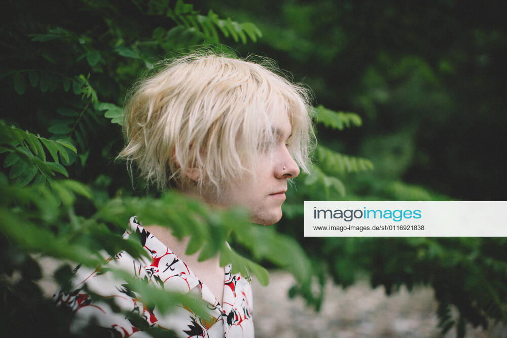 IMAGO Creative: Nächste Generation, Sozial- und klimabewusst Teen Boy With Bleach Blonde Hair Stands in Profile among Green Leaves Nevada City, CA, United States CR_CXBA210422-683370-01 ,model released, Symbolfoto