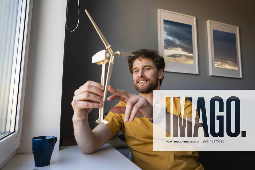 IMAGO Creative: Corporate: Klimaschutz, Digitalisierung und Urbanisierung IMAGO Creative: Klimawandel - Zukunft und Innovation Smiling businessman holding wind turbine model while sitting at home model released Symbolfoto property released VPIF03875