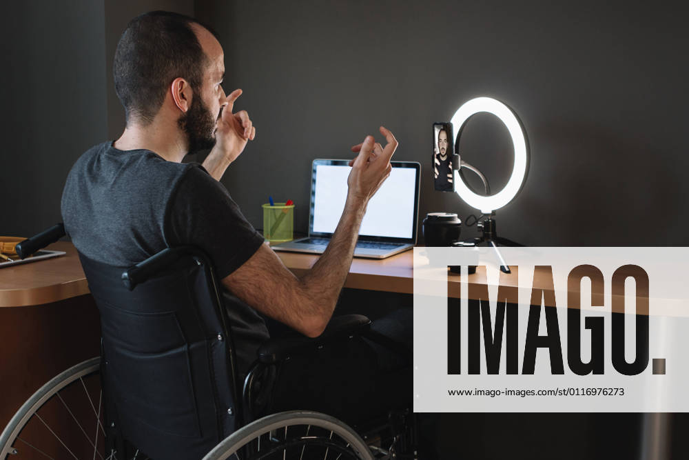 Vlogger filming through mobile phone with circular strobe tripod while sitting on wheelchair at studio model released Symbolfoto property released XLGF01348