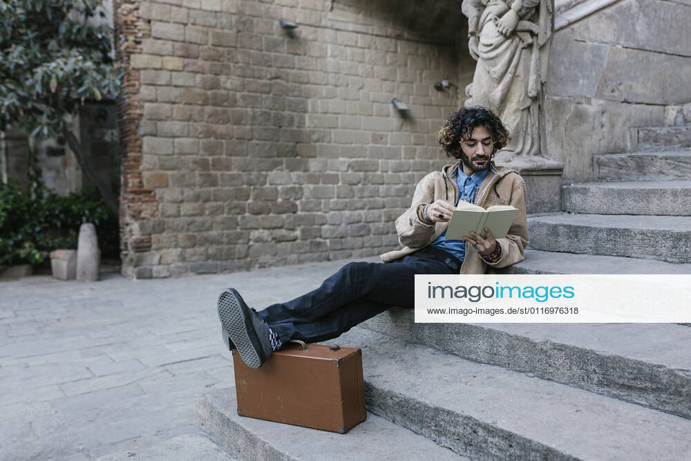 Young man with feet up reading book while sitting on steps model released Symbolfoto XLGF01383