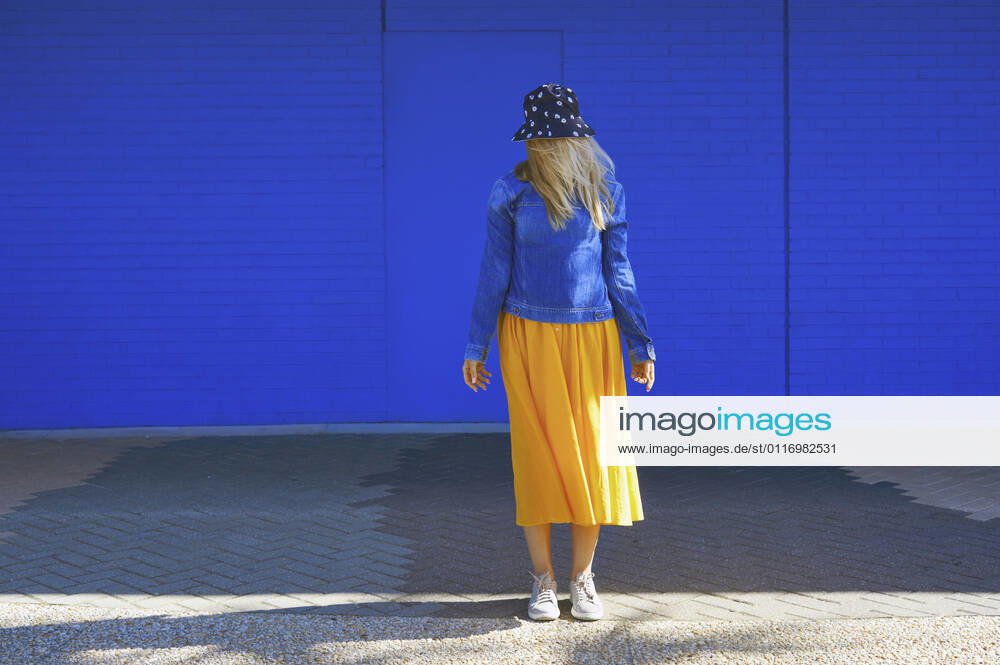 Blond woman wearing bucket hat standing in front of blue wall model released Symbolfoto AZF00278
