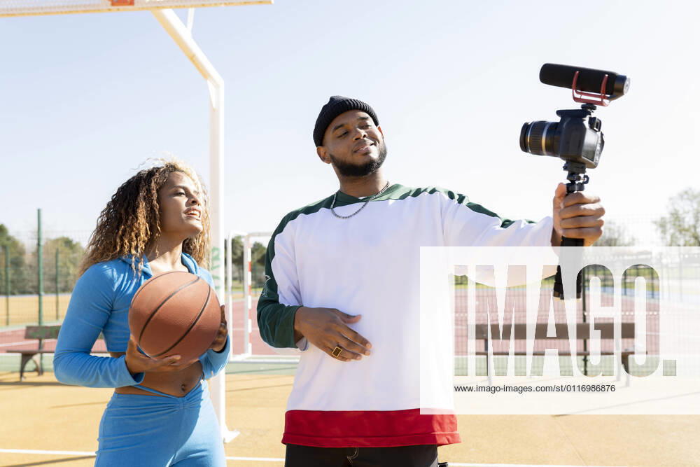 Male holding tripod with camera while vlogging with female friend on sports court model released Symbolfoto JCCMF01722