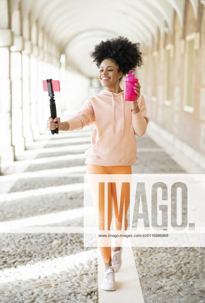 Smiling woman vlogging with smart phone while walking in arcade model released Symbolfoto JCCMF01778