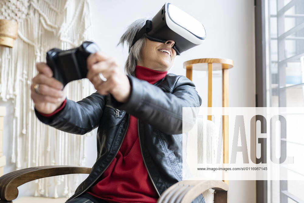 Smiling woman with game controller playing through virtual reality simulator at home model released Symbolfoto property released JCCMF01911